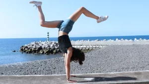 Frau am Strand fühlt sich fit und macht Handstand mit E.COOLINE Powercool SX3 Tanktop