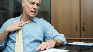 Banner mit Mann in Hemd und Krawatte, der sich an der Krawatte zieht um sie zu lockern, da ihm heiß ist